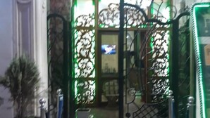 Entrada de un hotel con piso de baldosas, una planta en maceta y una puerta metálica decorativa.