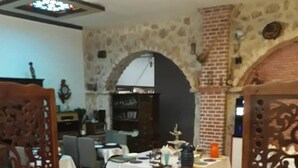 Un comedor con una mesa dispuesta para cuatro personas, rodeada de sillas. Se observa un biombo decorativo con intrincados diseños tallados. La habitación tiene una pared de piedra y una chimenea de ladrillo.