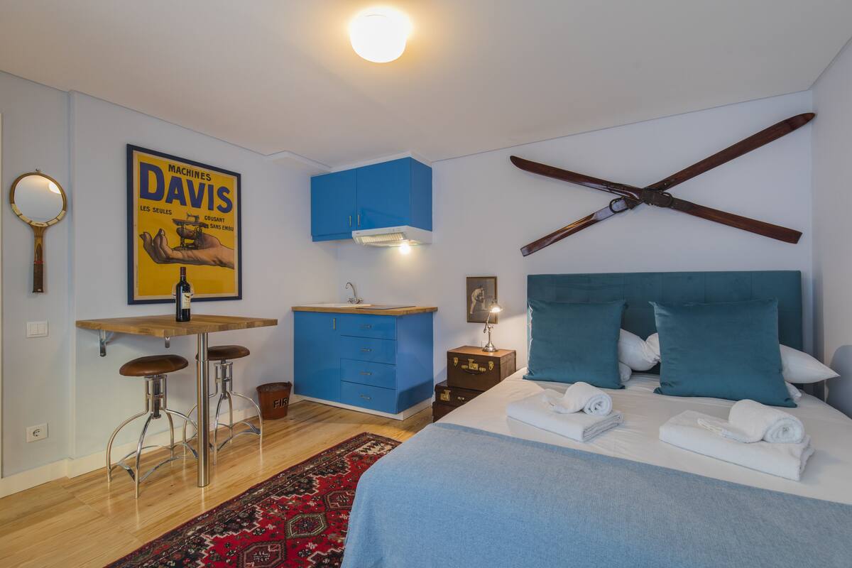 A bedroom with a bed, a desk with stools, a blue cabinet, and a ceiling fan.