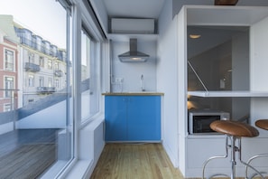 A compact kitchen with blue cabinets, a wooden floor, and a window overlooking a cityscape.