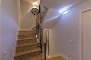 A wooden staircase with a clock on the wall, a light fixture, and a door at the end.