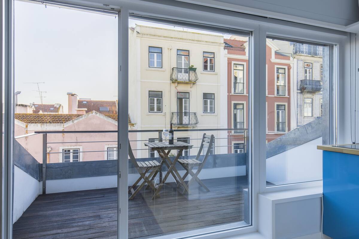 A balcony with a wooden table and chairs, a view of neighboring buildings, and a blue cabinet.