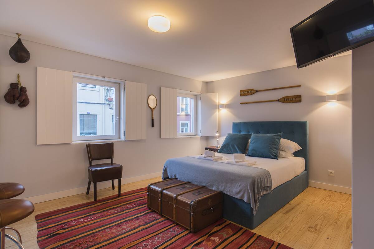 A bedroom with a bed, a chair, a suitcase, a television, and a window.