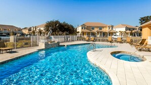 A swimming pool with a wooden deck, lounge chairs, and a fence.