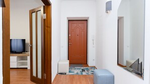 A hallway with a wooden door, a television on a desk, and a small seating area.