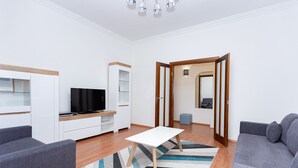 A modern living room with a flat-screen TV, grey sofas, a white coffee table, and a wooden floor.