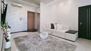 Ein modernes Wohnzimmer mit einem weißen Sofa, einem Glastisch und einem grauen Shaggy-Teppich.
