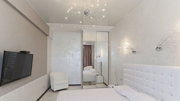 Ein modernes Schlafzimmer mit einem großen Bett, einem an der Wand montierten Fernseher, einem weißen Stuhl und einer Schiebetür zu einem Badezimmer.
