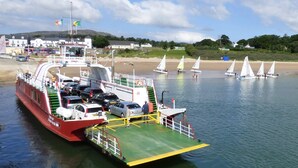 A ferry docked at a beach with sailboats in the background. - Rathmullan Holiday Homes (Rathmullan)