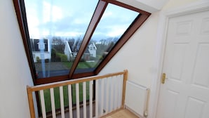 A room with a sloped ceiling, a wooden deck, and a view of houses through a large window. - Rathmullan Holiday Homes (Rathmullan)