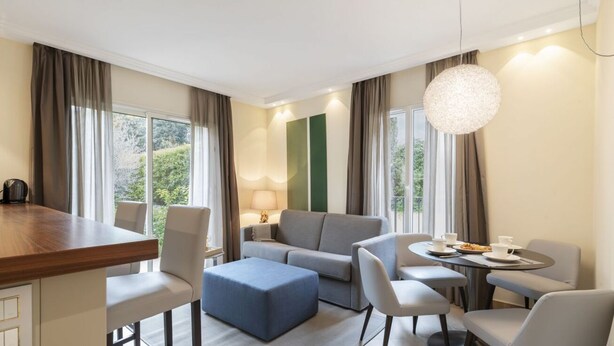 Et moderne hotelværelse med et træspisebord, en sofa, en blå skammel og et rundt bord med stole.