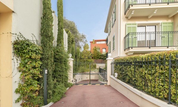 A narrow alleyway with a gated entrance, flanked by buildings with balconies and green shutters. - Suite Odyssée 001 (Saint Jean Cap Ferrat)