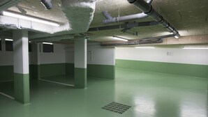 Eine leere Parkgarage mit grünen und weißen Wänden, Betonpfeilern und sichtbarer Lüftungsanlage an der Decke.