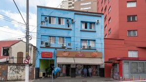 A blue building with a restaurant on the ground floor, a no parking sign, and a red building adjacent to it. - Hotel Sany (São Paulo)