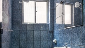 A bathroom with blue tiles, a toilet, a sink, and a window. - Hotel Sany (São Paulo)