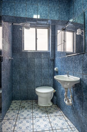 A bathroom with blue tiles, a toilet, a sink, and a window.
