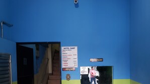 A hotel reception area with a blue wall, a reception desk, a staircase, and a price list on the wall. - Hotel Sany (São Paulo)