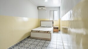 A small, narrow room with a bed, a window, and a wall-mounted air conditioner. - Hotel Sany (São Paulo)