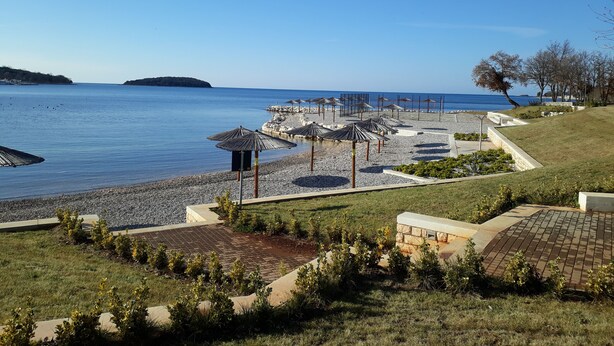 Um resort à beira-mar com uma praia de pedras, guarda-sóis e vista para o mar.