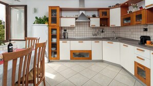 Uma cozinha moderna com armários brancos, detalhes em madeira, forno embutido e um espaço de refeições com cadeiras e mesa.