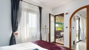 Quarto com cama, espelho grande e porta de vidro deslizante para área externa.