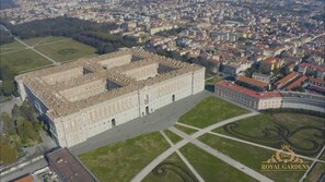 An aerial view of a large, historic building with symmetrical architecture, surrounded by well-maintained gardens and a dense urban area in the background. - Royal Gardens B&B Caserta (Caserta)