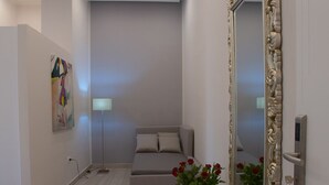 A modern living room with a grey sofa, a white console table with a bowl of fruit, a mirror with an ornate frame, and a painting on the wall. - Royal Gardens B&B Caserta (Caserta)
