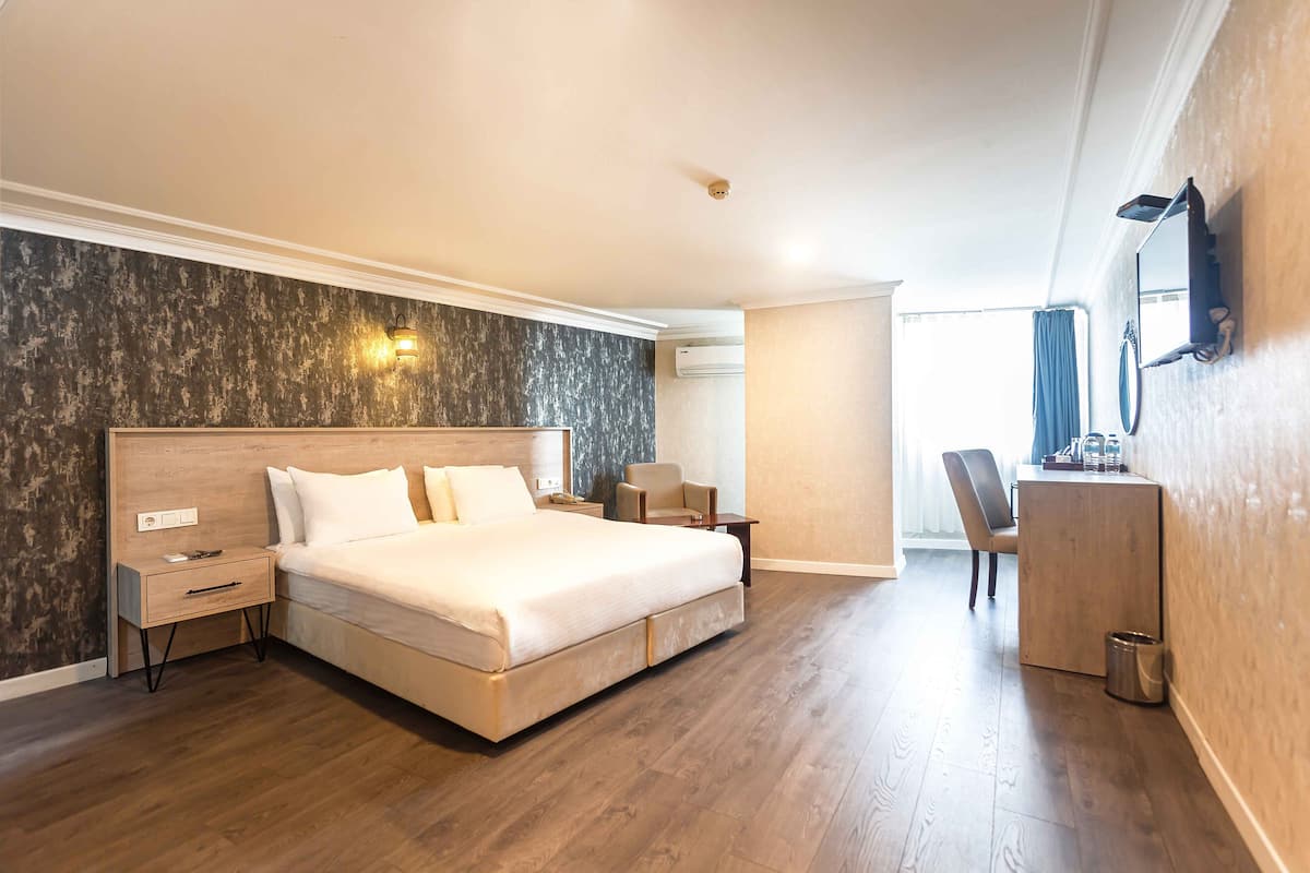 A hotel room with a large bed, a desk with a chair, a mirror, and a wall-mounted TV.