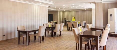 A spacious conference room with multiple tables and chairs, wooden flooring, and recessed ceiling lights.