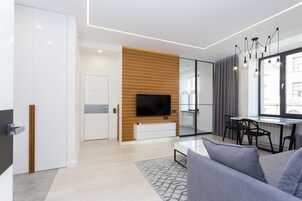 Ein modernes Wohnzimmer mit Flachbildfernseher, einer Holzvertäfelung, einer Essecke mit Glastrennwand und einem großen Fenster mit Vorhängen.