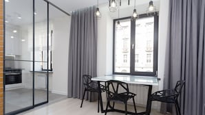 A modern kitchen with a glass partition, a dining table with chairs, and a view of buildings through a window. - MinskLux Apartment on Nezavisimosti ave. 13 (Minsk)