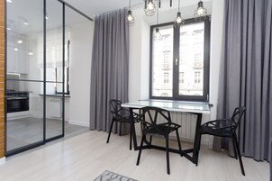 Eine moderne Küche mit Glastrennwand, einem Esstisch mit Stühlen und Blick auf Gebäude durch ein Fenster.