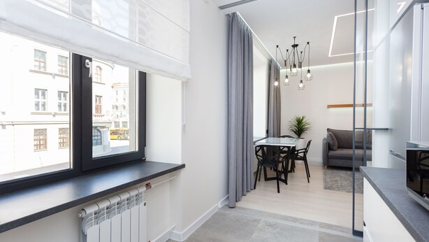 A modern kitchen with a large window, a dining area with a table and chairs, and a living area with a sofa and a plant. - MinskLux Apartment on Nezavisimosti ave. 13 (Minsk)