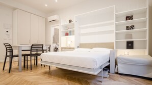 A modern bedroom with a bed, bedside tables, a desk with chairs, and built-in shelving. - Calzolerie studio (Bologna)