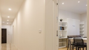 A hallway with a wooden floor leading to a room with a desk and chair. - Calzolerie studio (Bologna)