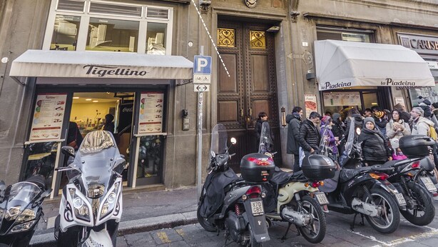 A building with an entrance labeled "Tigellino," a parking sign, and several parked motorcycles. - Calzolerie studio (Bologna)