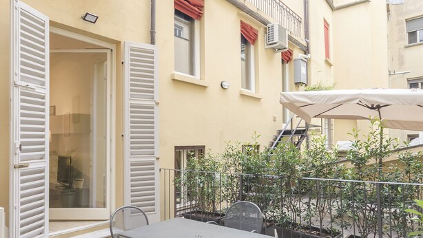 Un patio con mesa y sillas, una zona cubierta y plantas en macetas.