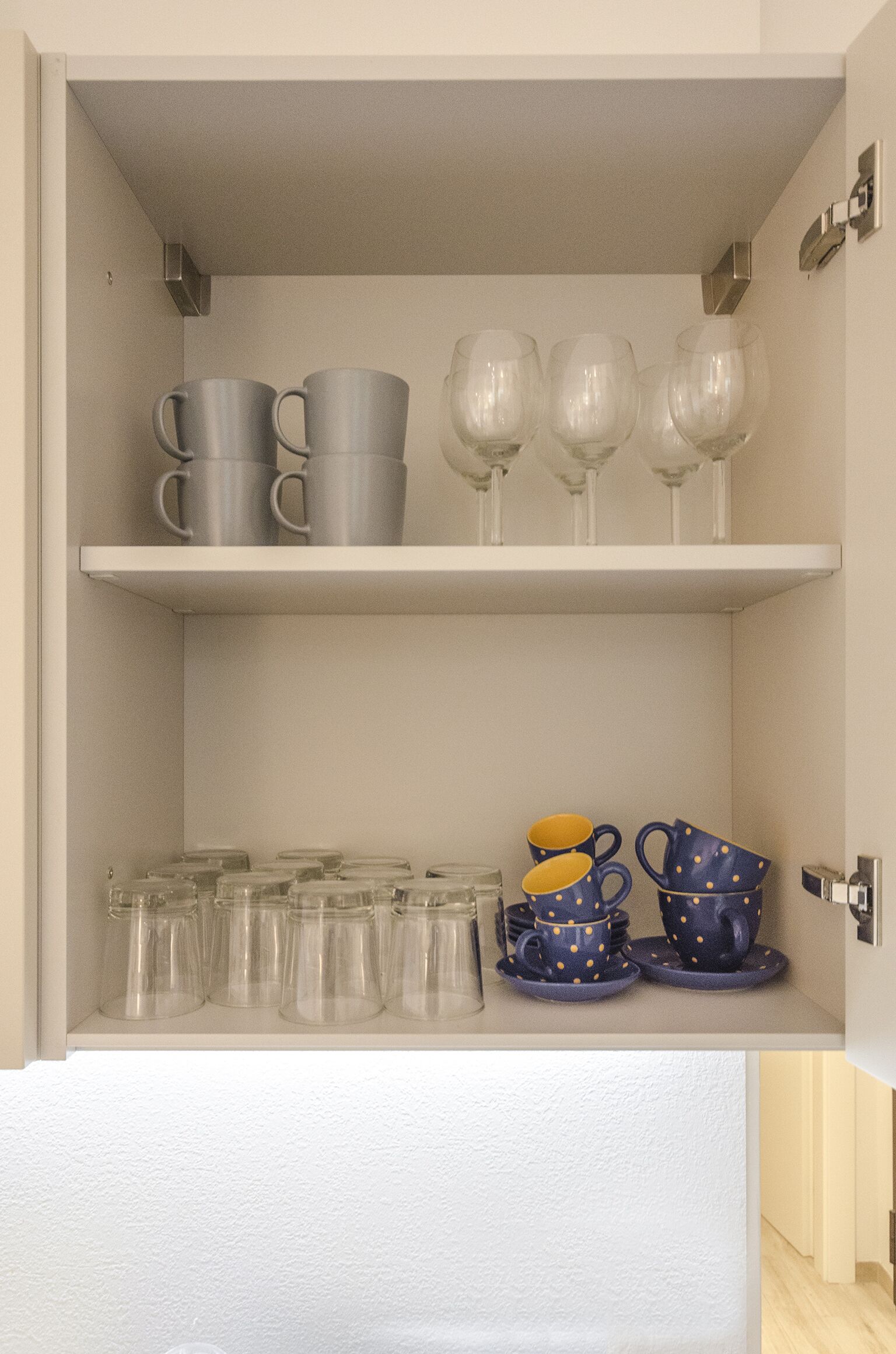 Una cocina con dos repisas; la repisa superior contiene tazas y copas de vino, y la repisa inferior tiene vasos transparentes y tazas azules con lunares amarillos.