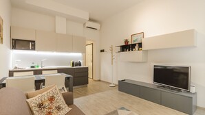 Una sala de estar moderna con un sofá, un televisor de pantalla plana y una cocina equipada con microondas y hervidor.