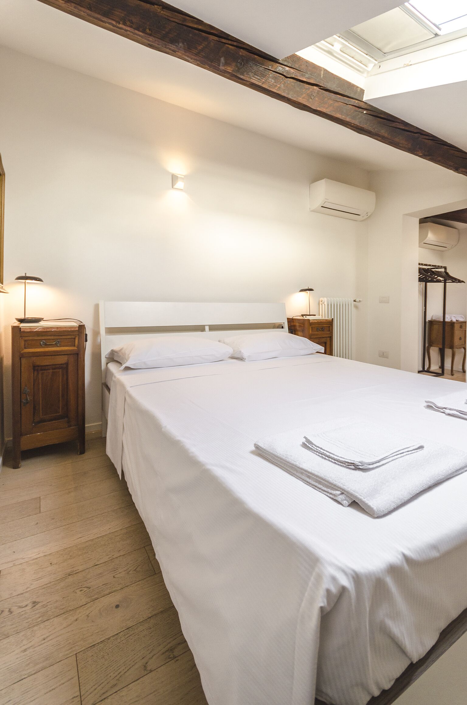 A neatly made bed in a room with wooden beams on the ceiling, a radiator, and a wall-mounted air conditioner.