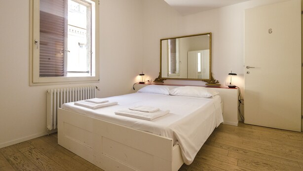 A bedroom with a bed, a window, a mirror, a radiator, and a door. - Appartamento del Nettuno (Bologna)