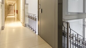 A modern hotel corridor with a staircase, a glass elevator, and a clean, well-lit interior. - Appartamento del Nettuno (Bologna)