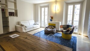 A modern living room with a wooden coffee table, a white sofa, a colorful bean bag chair, and a blue rug.