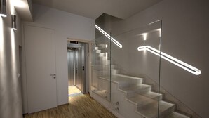 A modern interior with a wooden floor, a glass staircase with integrated lighting, and an elevator in the background.