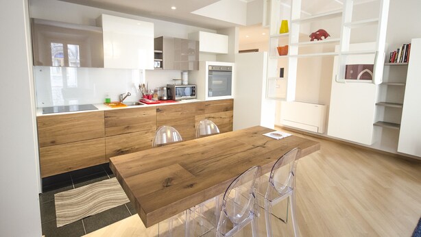 A modern kitchen with wooden cabinets, a wooden dining table, and clear chairs.