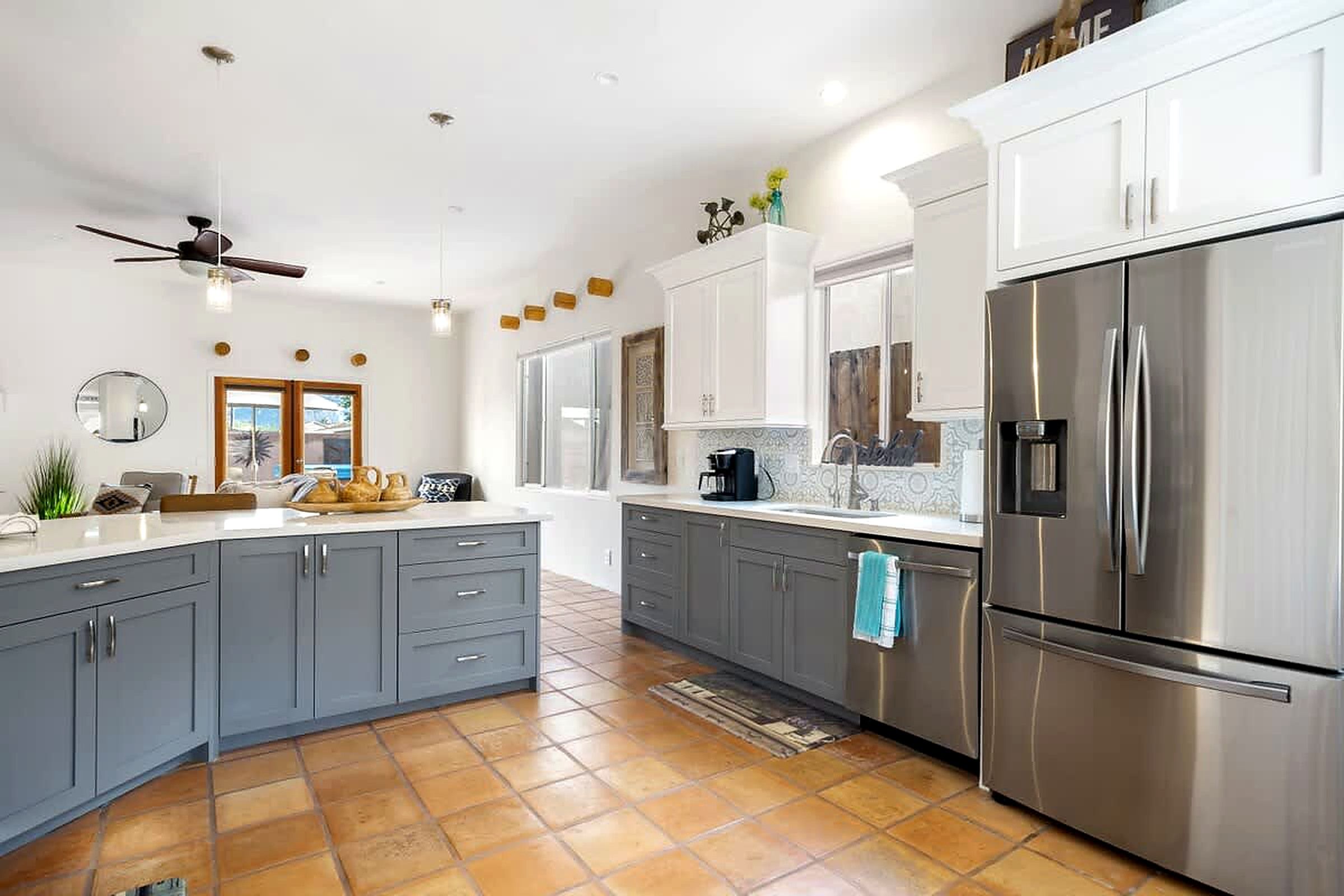 A modern kitchen with grey cabinets, a stainless steel refrigerator, and a ceiling fan.