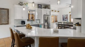 A modern kitchen with white cabinetry, a central island, and pendant lighting. - Hacienda Getaway Pool, Hot Tub, & Steps to trails. (La Quinta)