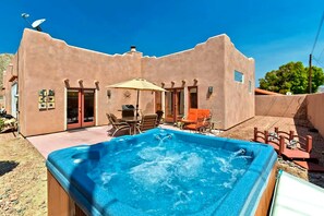 A hot tub in a backyard with a patio table and chairs, surrounded by a stucco building with a satellite dish. - Private Pool & Hot Tub · Game Room · Near Trails (La Quinta)