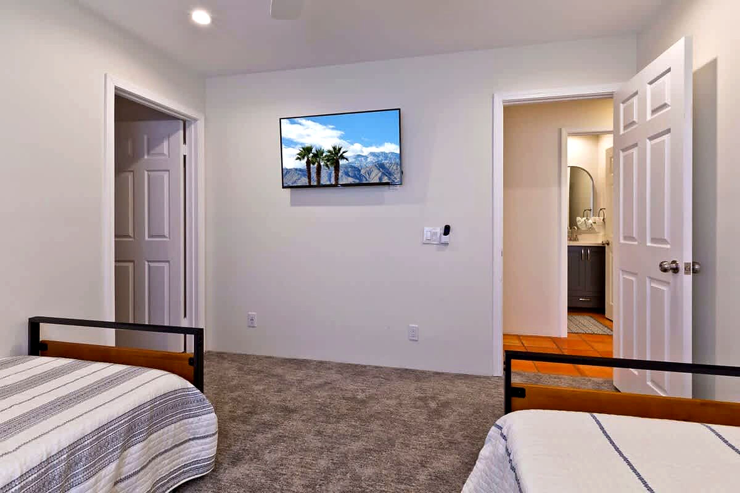 Un dormitorio con dos camas, un televisor en la pared y un baño visible a través de una puerta abierta.