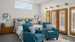 A bedroom with a bed, two chairs, a nightstand, a mirror, and a window. - Hacienda Getaway Pool, Hot Tub, & Steps to trails. (La Quinta)